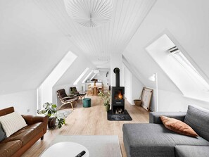 Un loft spacieux avec de hauts plafonds, des fenêtres de toit, une cheminée centrale et un coin salon confortable avec des canapés en cuir et une table à manger.