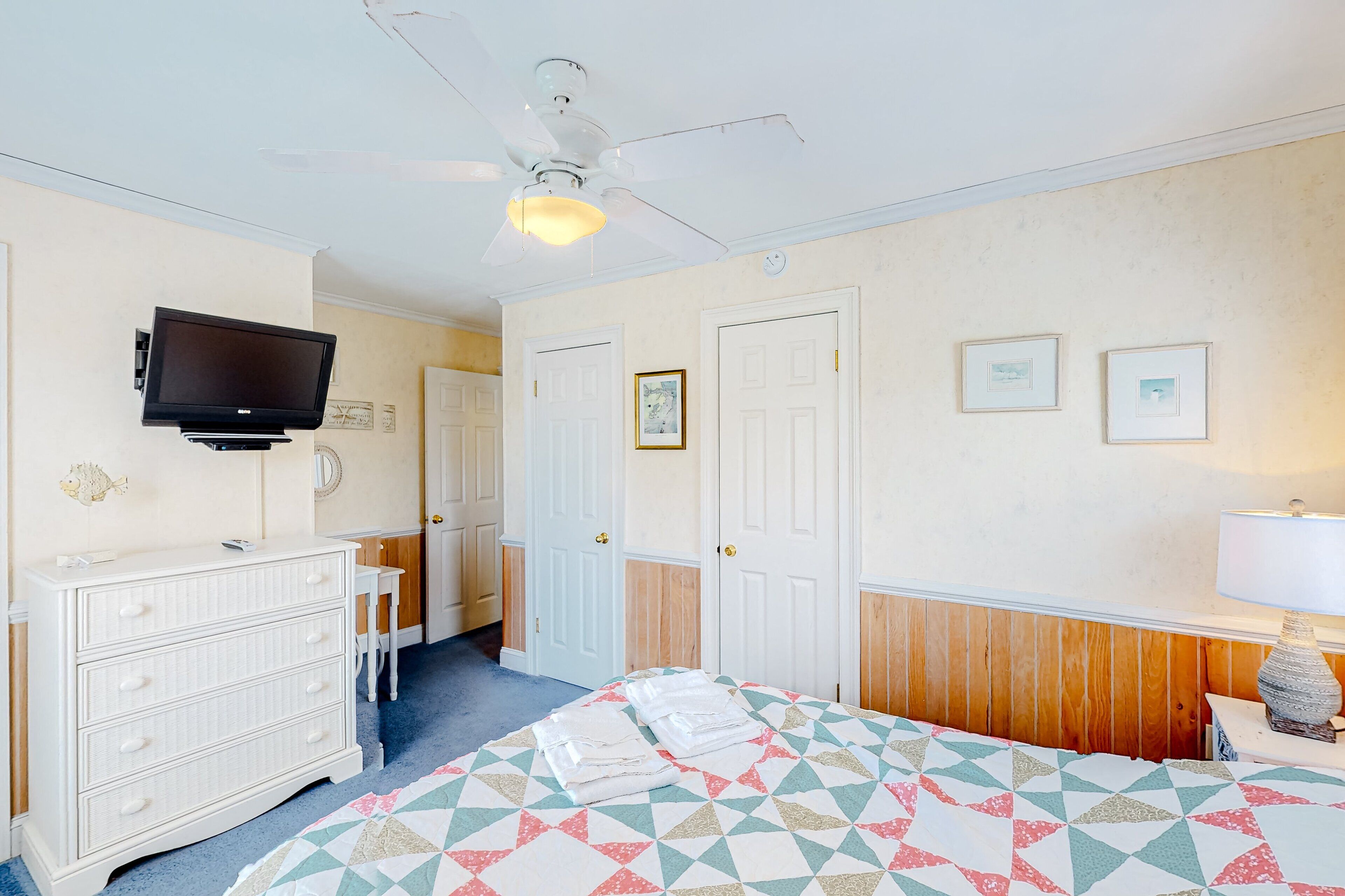 Ein Hotelzimmer mit Bett, Kommode, Fernseher, Deckenventilator und einer Tür.
