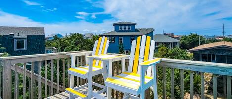 Une terrasse en bois avec des fauteuils Adirondack blancs et jaunes et un banc turquoise.