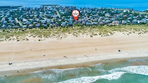 Vista aérea de uma vila costeira com propriedades à beira-mar, uma praia e ondas do oceano.