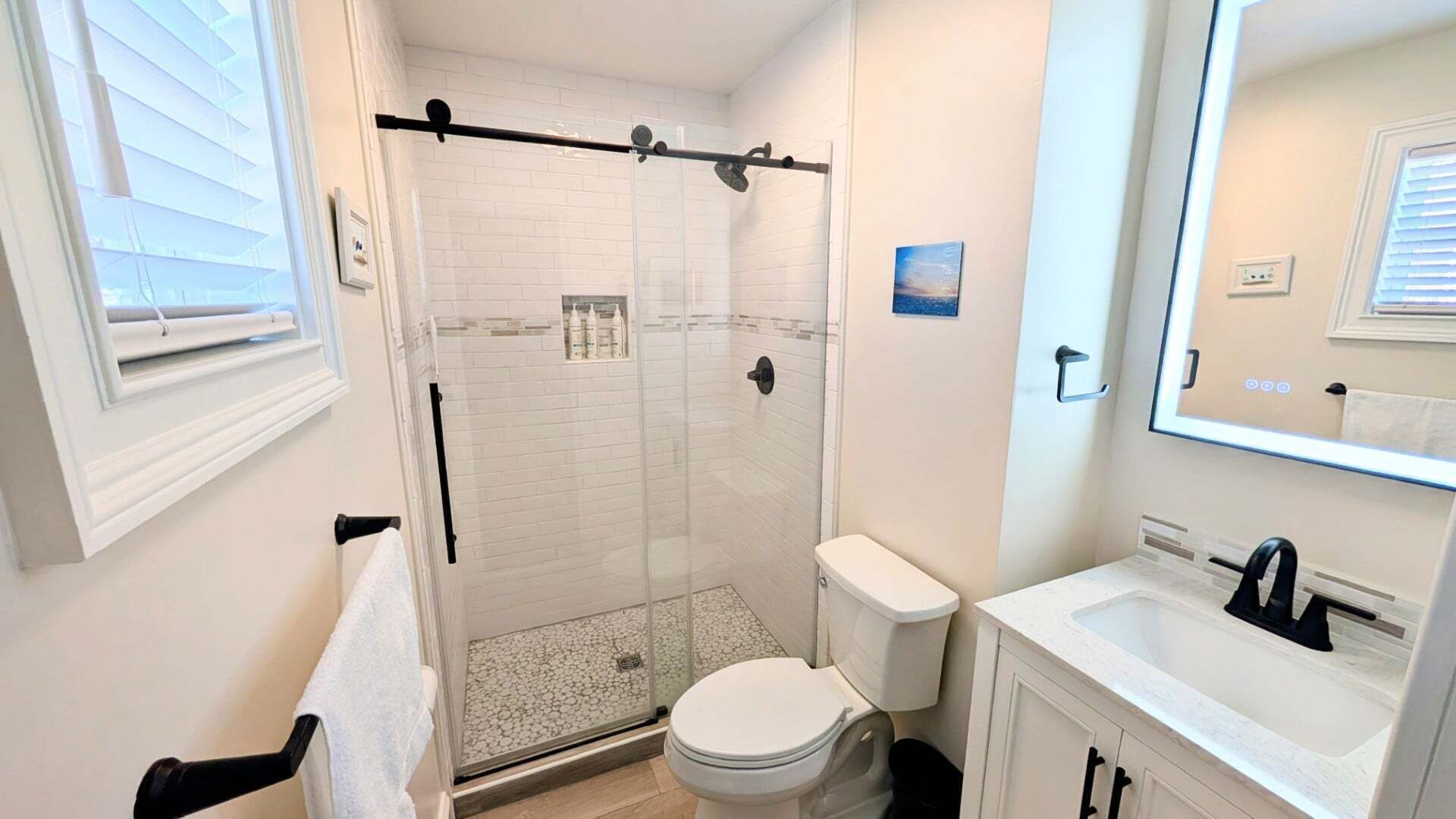 Un bany amb dutxa de vidre, vàter, rentamig i mirall.