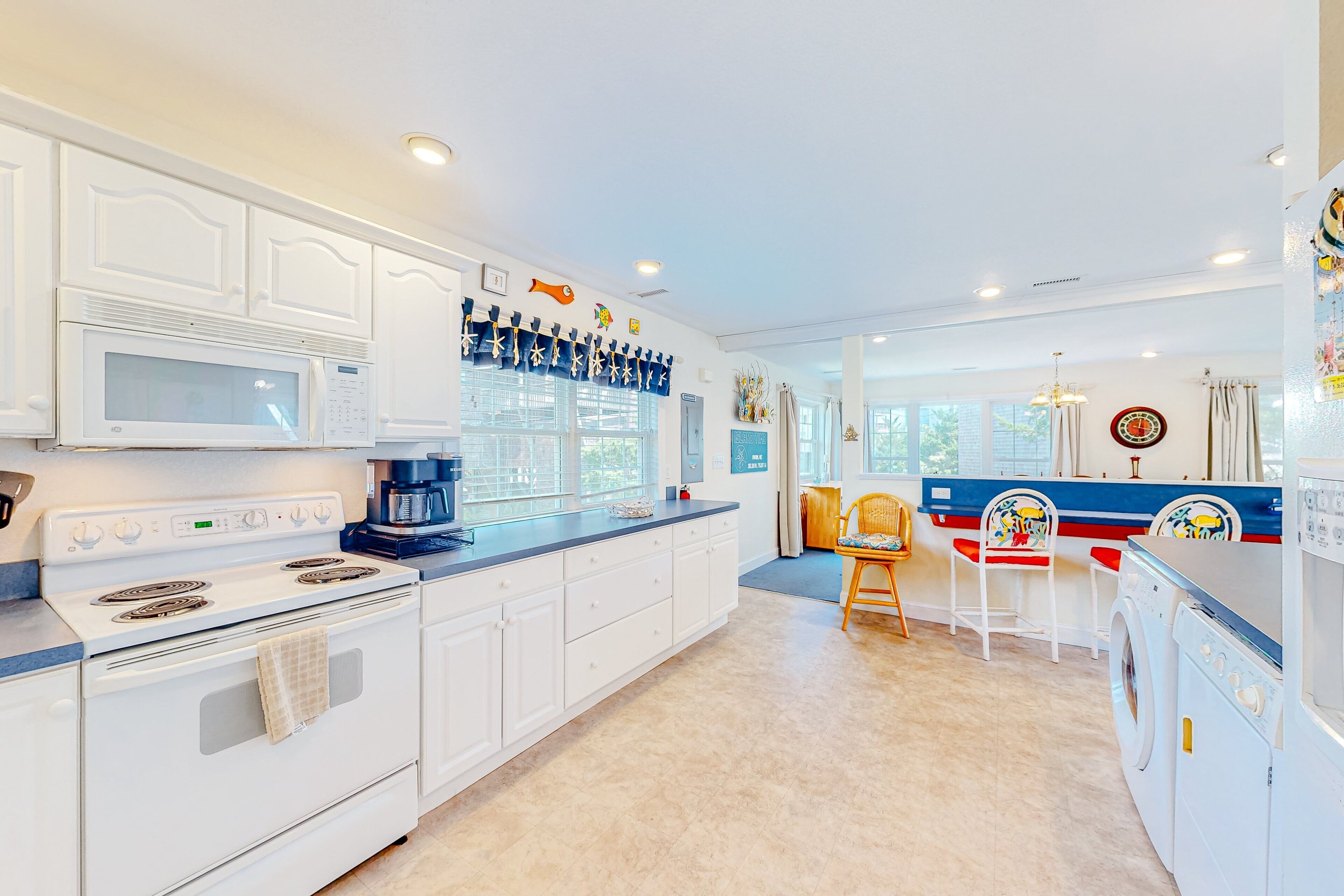 A kitchen with white cabinets, a microwave, stove, and a coffee maker. There is a dining area with a table and chairs.