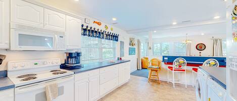 A kitchen with white cabinets, a microwave, stove, and a coffee maker. There is a dining area with a table and chairs.