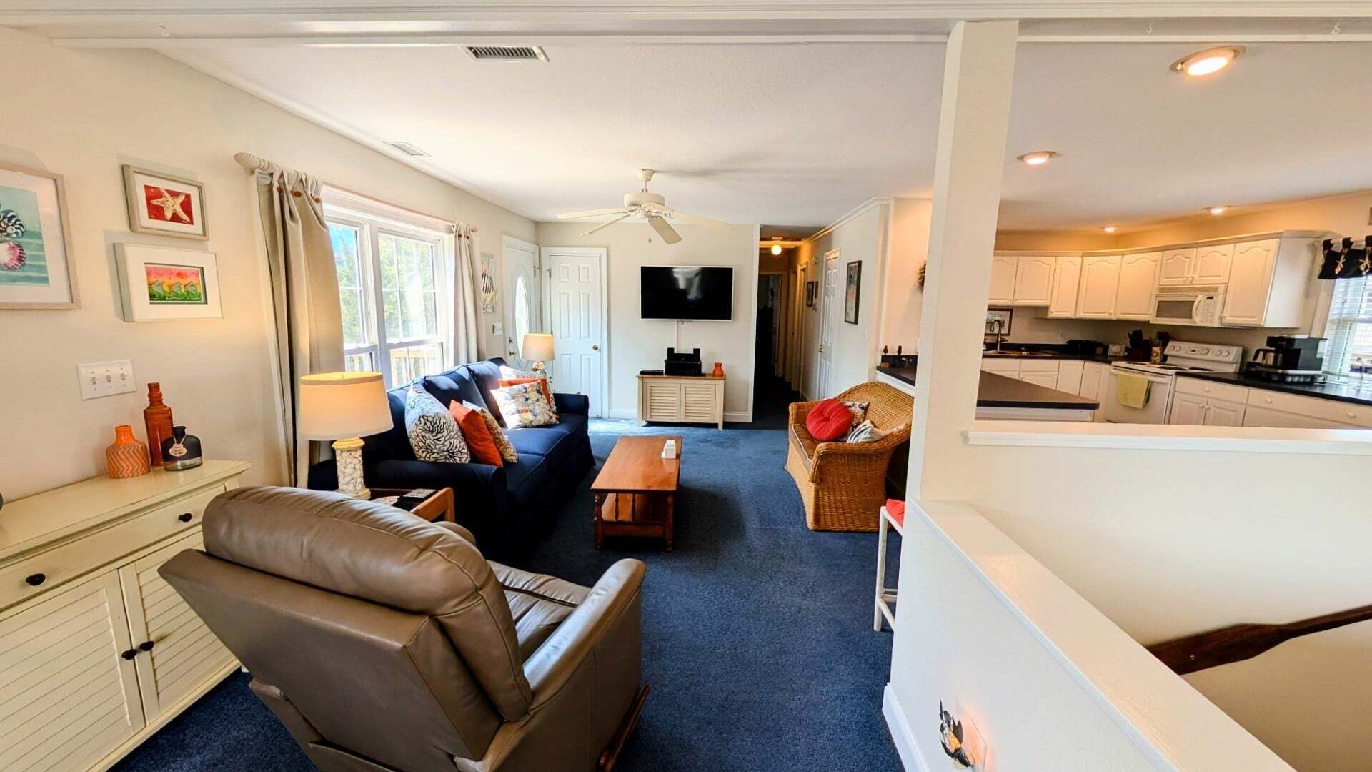 Sala de estar con sofá, una silla, televisor y área de cocina con armarios y electrodomésticos.