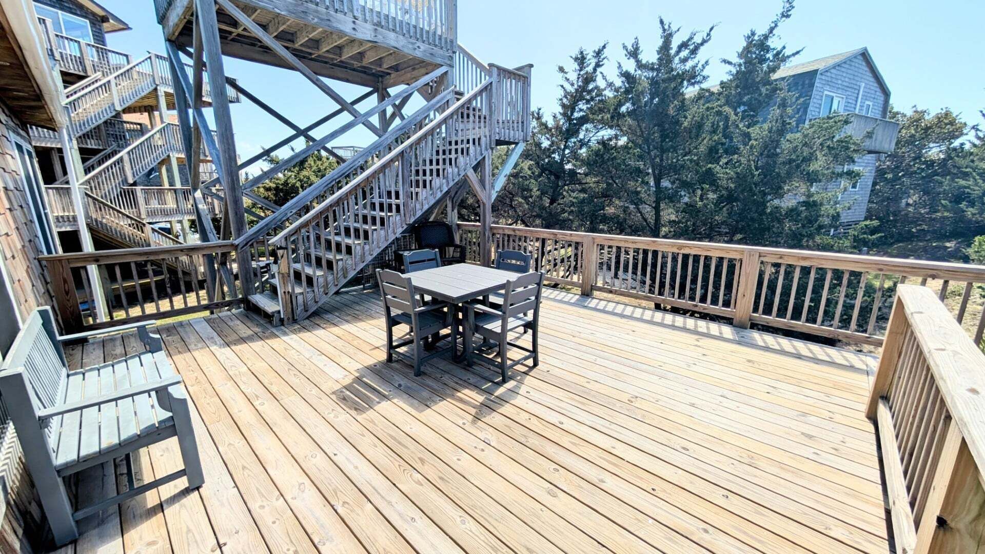 Eine Holzterrasse mit Tisch und Stühlen, eine Treppe und Blick auf Bäume und Gebäude.