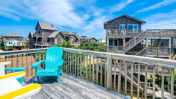 Um deck de madeira com uma cadeira Adirondack azul e uma cadeira amarela e branca.