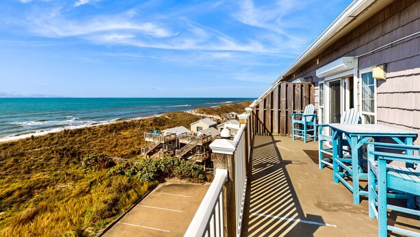 Un hotel sulla costa con un balcone vista spiaggia, edifici in legno e area salotto all'aperto.