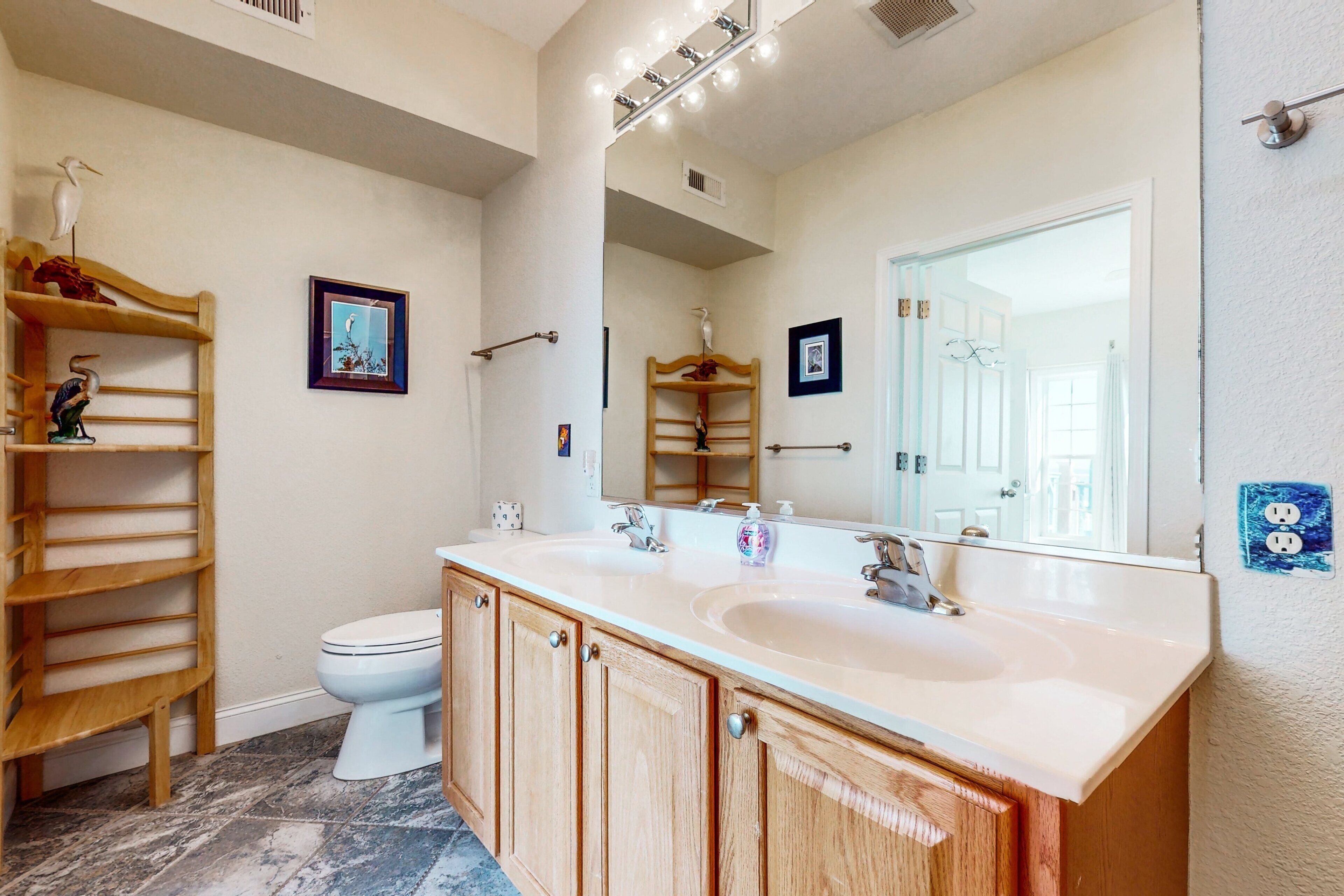 A bathroom with a wooden vanity, two sinks, a toilet, and a mirror.