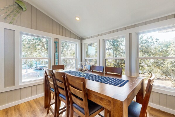 A dining area with a wooden table and chairs, large windows, and a view of the outdoors. - Dog-friendly coastal home with large yard and close to beach (Supply)