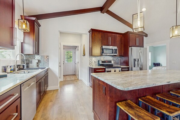 A modern kitchen with wooden cabinets, stainless steel appliances, and a marble island with bar stools.