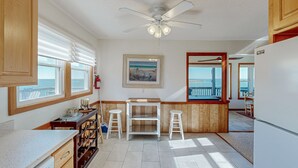 A kitchen with a ceiling fan, wooden cabinets, a wine rack, and a view of the ocean through large windows. - Sound FX 437: Sound-front w/shared pool (Avon)
