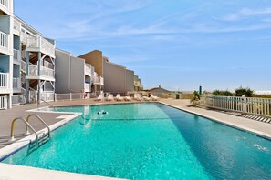 A swimming pool with a wooden deck, white railings, and lounge chairs.
