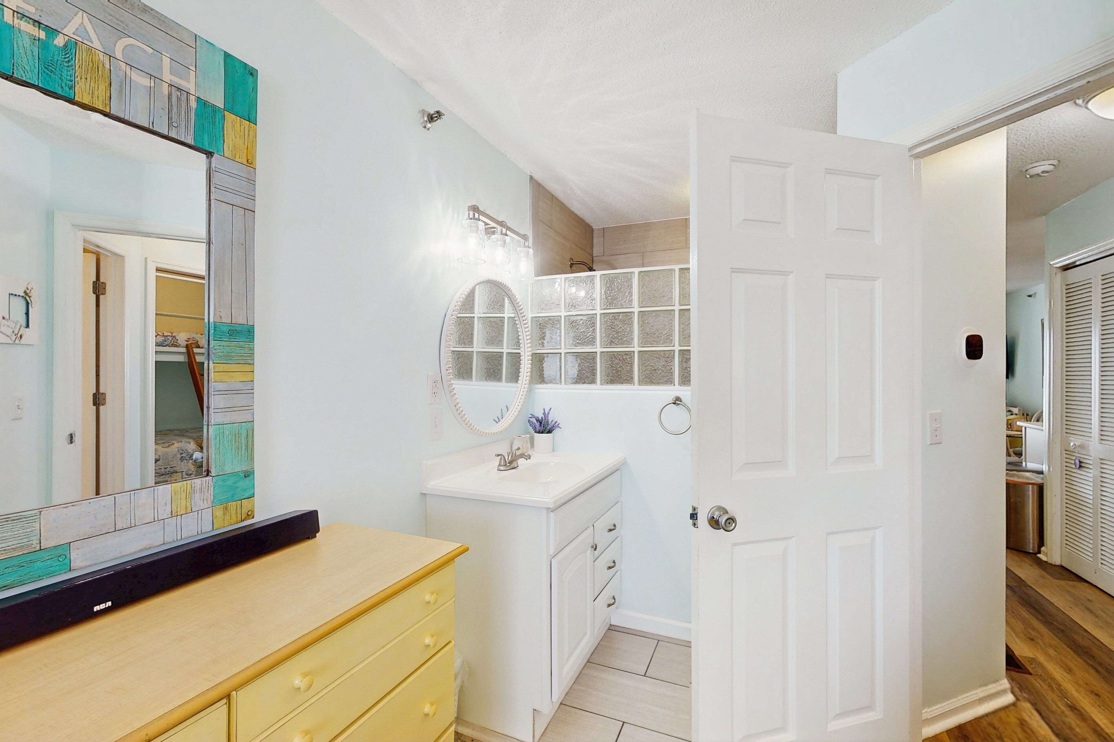 Une salle de bain avec un meuble-lavabo blanc, un miroir, un évier et un espace douche.