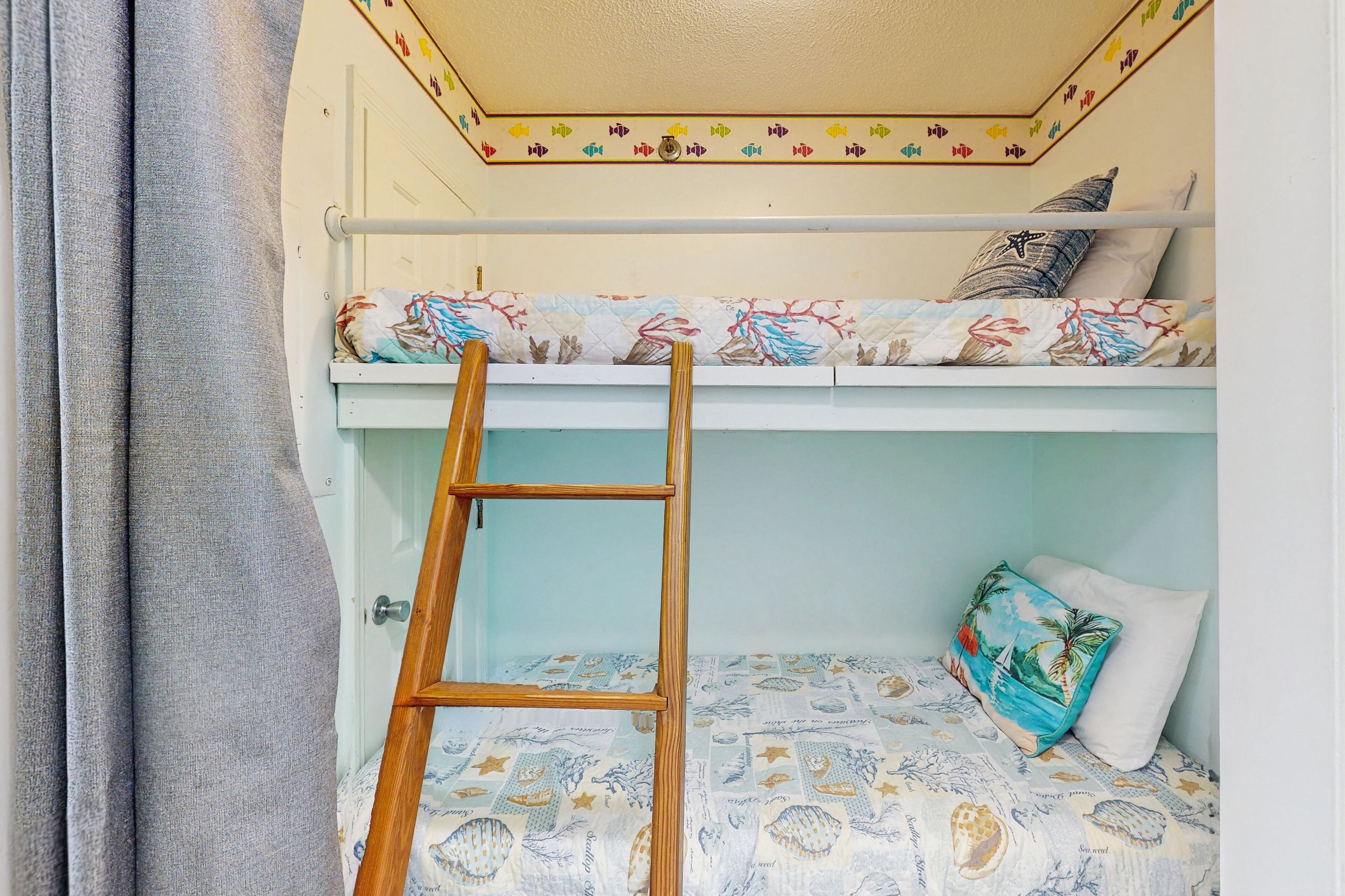 A bunk bed with a ladder, a patterned bedspread, and a pillow with a tropical design.