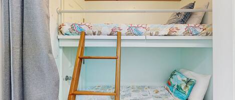 A bunk bed with a ladder, a patterned bedspread, and a pillow with a tropical design.