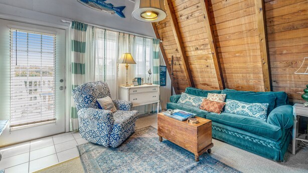 Un dormitorio estilo loft acogedor con techo inclinado, un sillón estampado, un sofá color turquesa y una mesa de centro de madera.