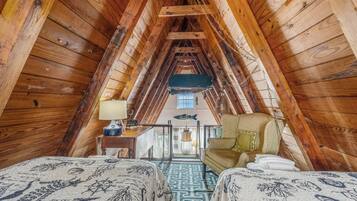 A cozy attic bedroom with wooden beams, a desk, and two beds with patterned bedding.