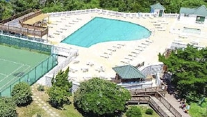Une piscine entourée d’une terrasse, un court de tennis et un petit pavillon.