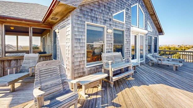 Une terrasse en bois avec des sièges extérieurs et de grandes fenêtres.