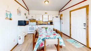 A compact kitchen with white cabinets, a microwave, and a coffee maker. There is a dining table with chairs and a patterned tablecloth.