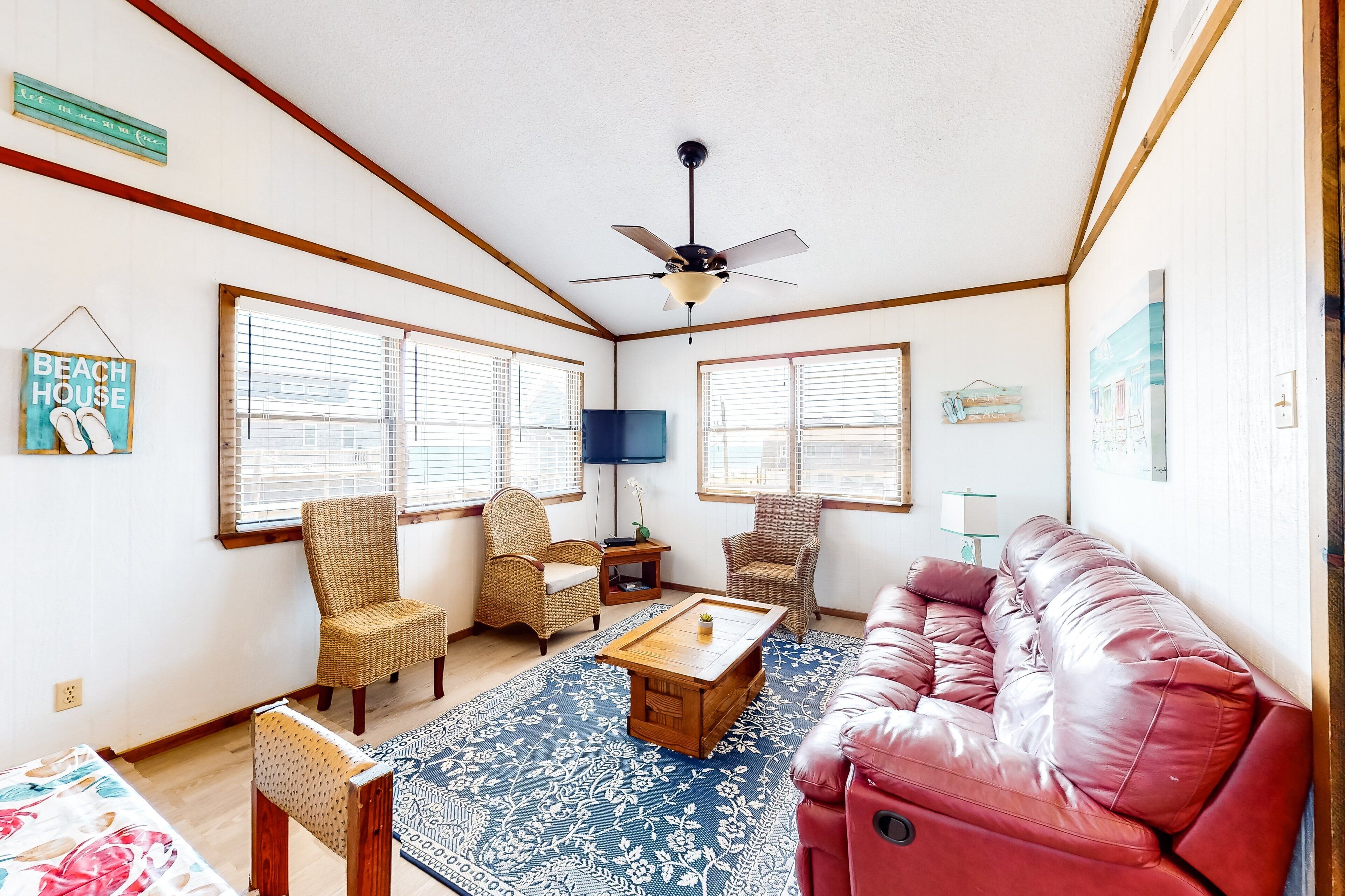 A living room with a red leather couch, wicker chairs, a coffee table, and a ceiling fan.