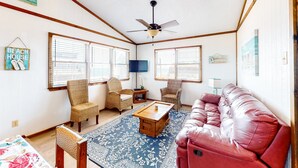 A living room with a red leather couch, wicker chairs, a coffee table, and a ceiling fan.