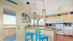 Cucina con zona bar, pavimento in legno e vista sulla spiaggia attraverso una porta.
