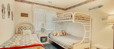 A room with a bunk bed, a single bed, a bedside table, a lamp, and a small wicker basket.