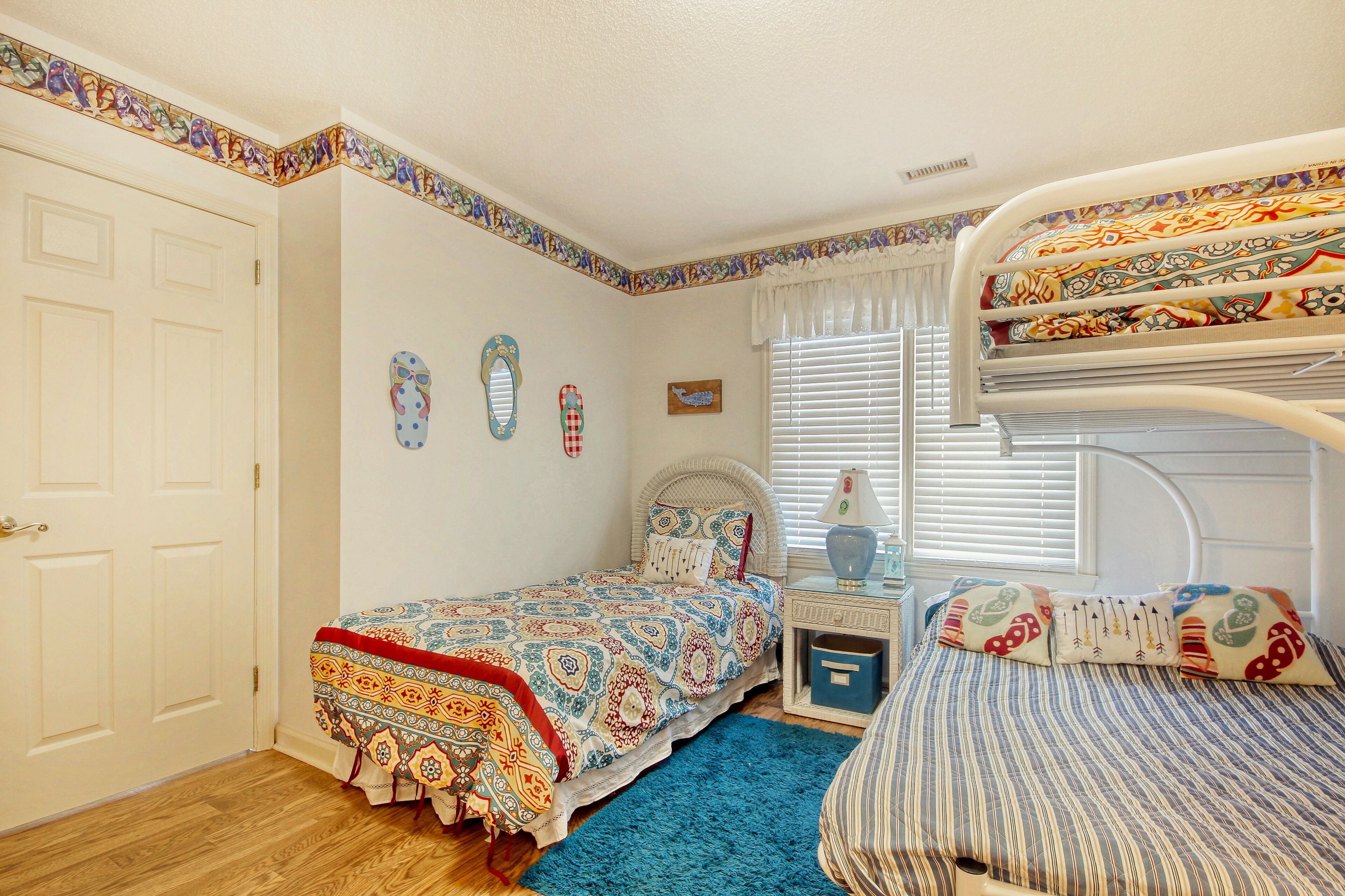 Une chambre avec un lit superposé, un lit simple, une table de chevet, une commode et une fenêtre avec des stores.