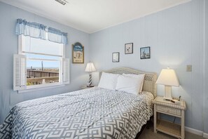 Un dormitorio con cama, dos mesitas de noche, una ventana con contraventanas y decoración en la pared.