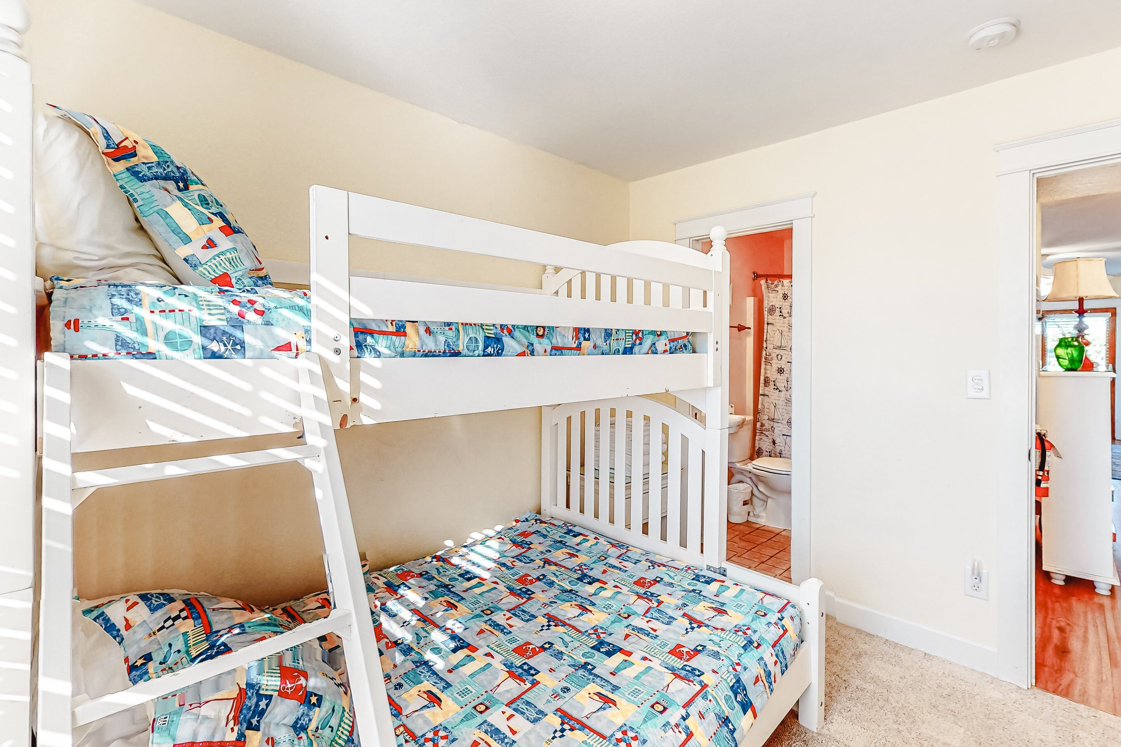 A bunk bed with a colorful quilt, a white door, and a visible bathroom with a toilet.