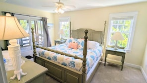 A bedroom with a four-poster bed, two bedside tables, a ceiling fan, and windows with curtains.