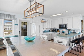A modern kitchen with white cabinets, a glass island, and a hanging light fixture. - Barefeet Retreat: Oceanfront home with a Private Beach Access and Spacious Covered Porches (Holden Beach)