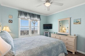 A bedroom with a bed, a dresser, a television, a window with blinds, and a ceiling fan. - Barefeet Retreat: Oceanfront home with a Private Beach Access and Spacious Covered Porches (Holden Beach)
