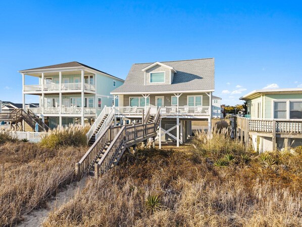 A beachfront property with multiple-story houses, a wooden staircase, and a sandy path leading to the beach. - Barefeet Retreat: Oceanfront home with a Private Beach Access and Spacious Covered Porches (Holden Beach)