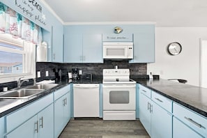 Une cuisine avec des meubles de couleur bleu clair, un four à micro-ondes blanc, une cuisinière blanche et un plan de travail noir.