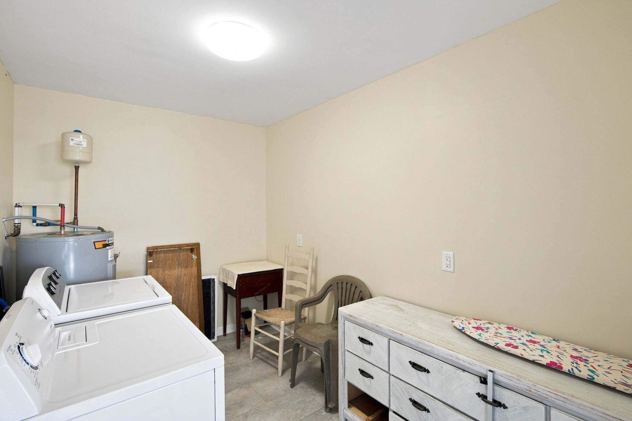 A laundry room with a washing machine, a dryer, a water heater, and a small table with a chair.