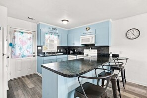 A modern kitchen with blue cabinets, a central island, bar stools, a microwave, and a clock on the wall.