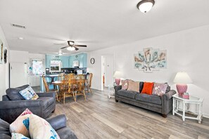A modern living room with a grey sofa, wooden chairs, and a dining area with a table and chairs.