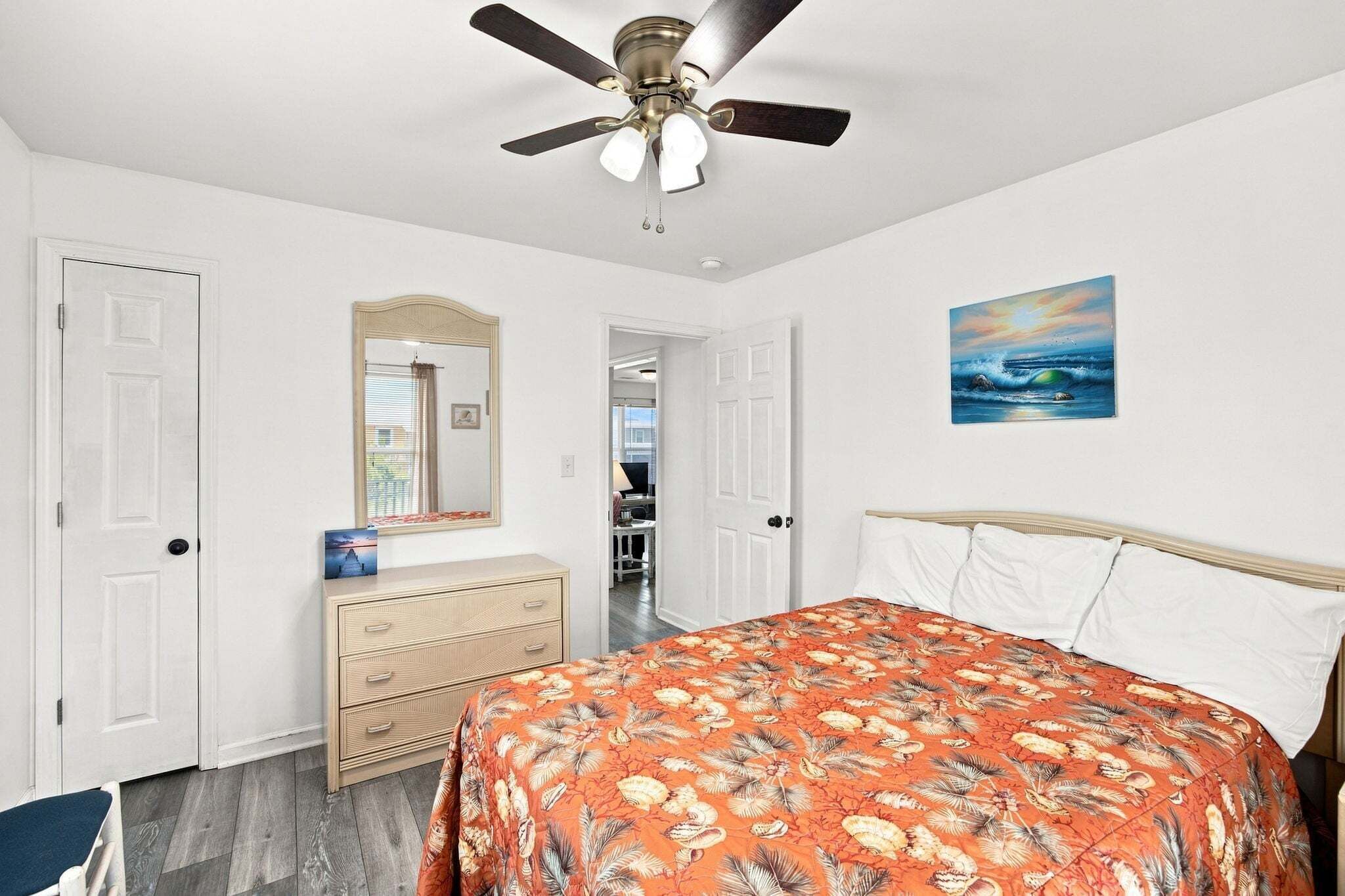 Ein Schlafzimmer mit Bett, Schminktisch, Deckenventilator und einem Bild an der Wand.