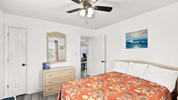 Een slaapkamer met een bed, een dressoir, een plafondventilator en een schilderij aan de muur.