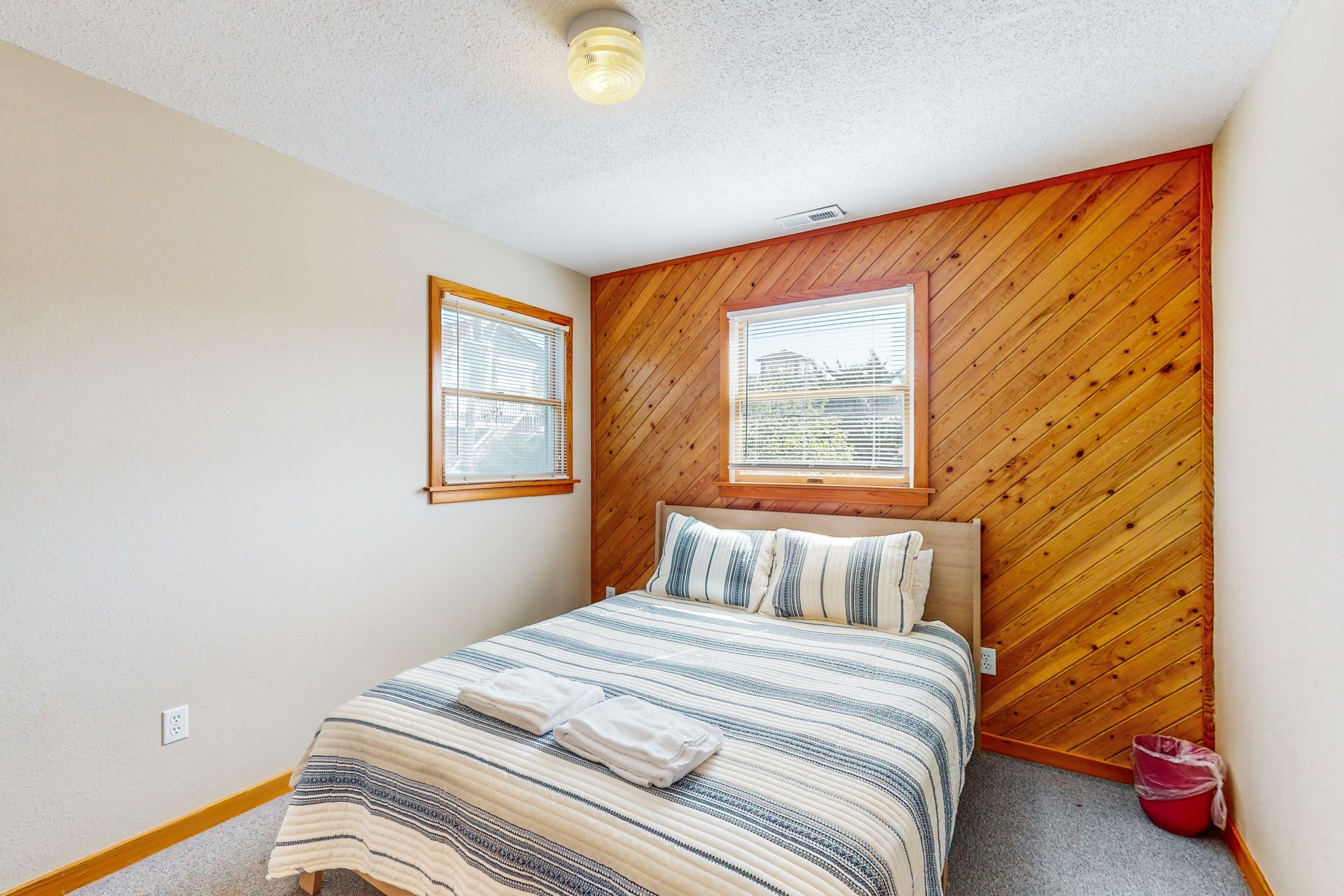 Une chambre à coucher avec un lit, deux fenêtres, un lambris en bois et un luminaire au plafond.