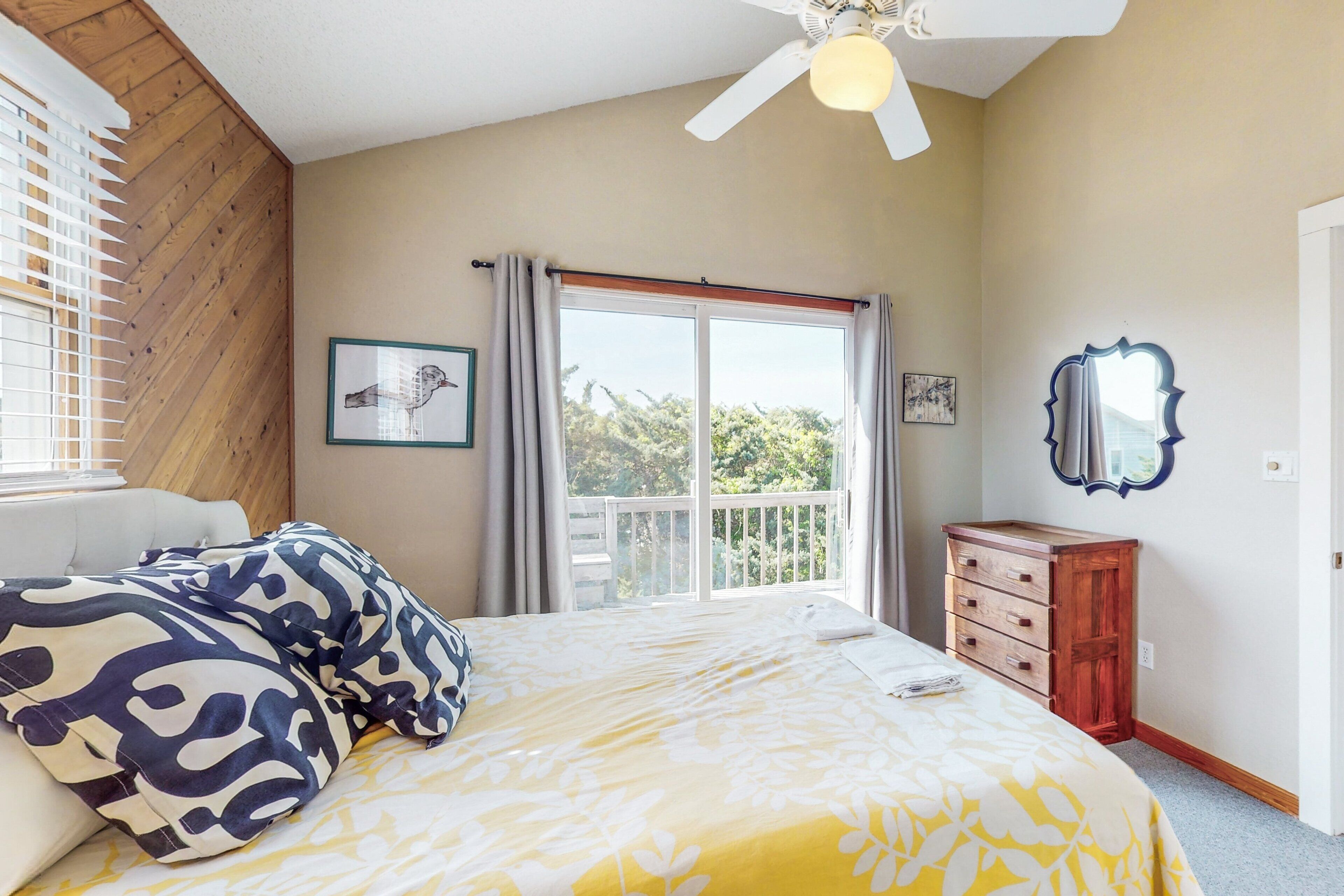 Une chambre à coucher comprenant un lit, une commode, un ventilateur de plafond et une fenêtre avec des rideaux.