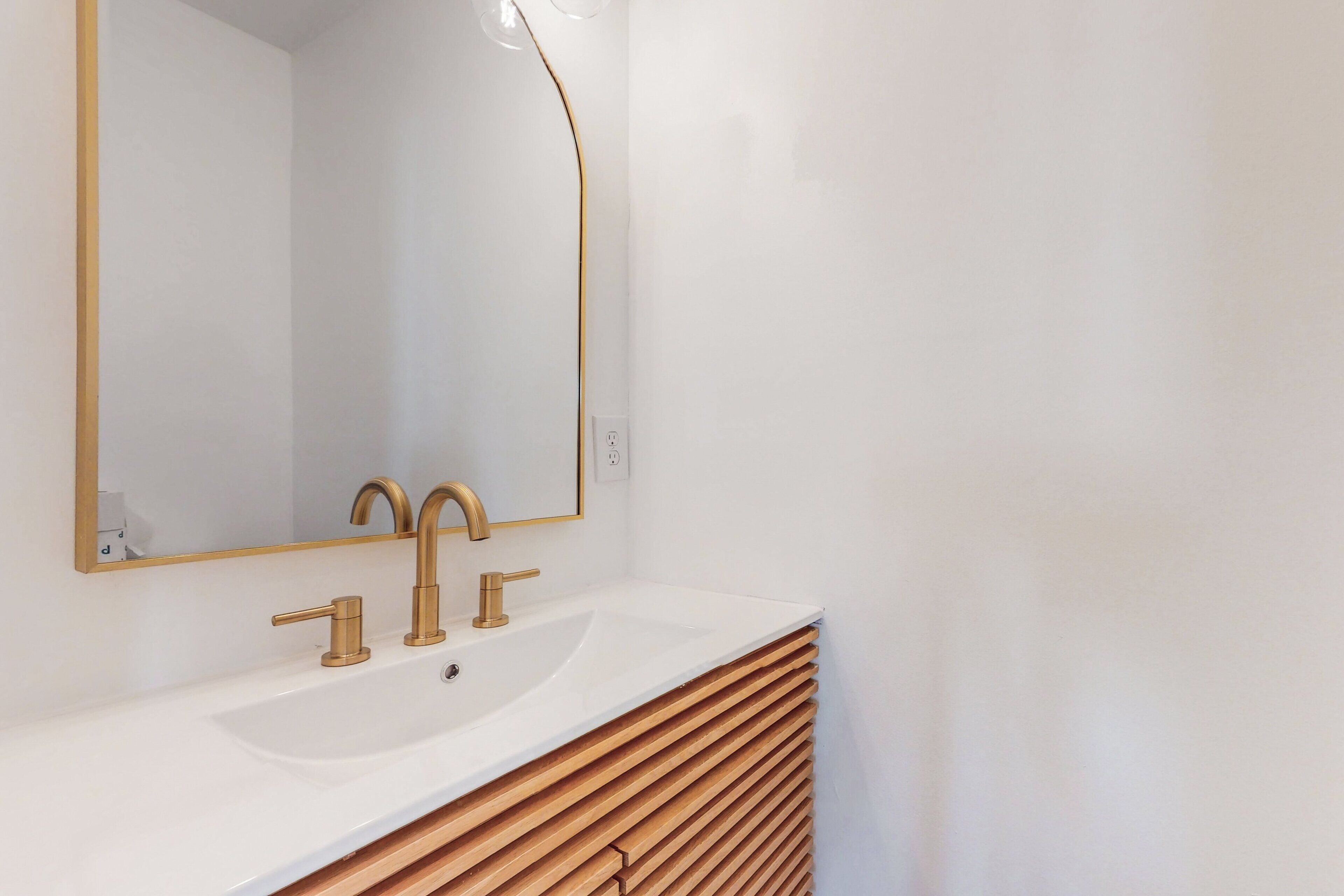 Une salle de bain avec un lavabo blanc, des robinets dorés et un grand miroir.