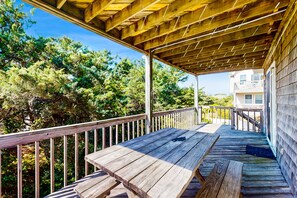 A wooden deck with a railing, overlooking a forested area. - Ocean-view home with amazing sunset vista, pool access, steps to beach boardwalk (Avon)