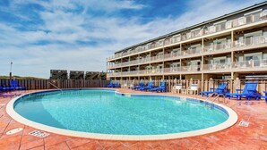 Una piscina con sillas azules y un edificio con balcones al fondo.