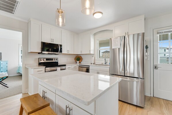 A modern kitchen with white cabinetry, stainless steel appliances, and a large island. - Beachfront Home with Free WiFi, Washer/Dryer, AC, & Deck - Dogs Welcome (Holden Beach)