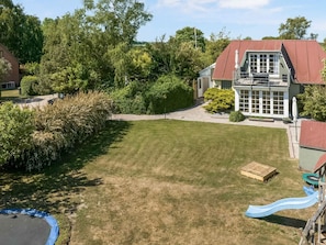 A backyard with a lawn, a trampoline, a slide, and a house with a red roof and large windows. - 5 Star Holiday Home in Otterup (Otterup)