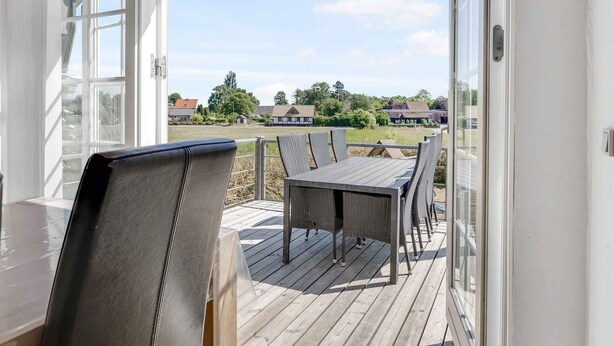 Een overdekt terras met een tafel en stoelen, met op de achtergrond huizen en groen.