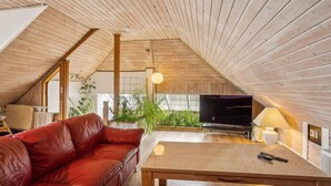 Een knus loft-stijl verblijf met een schuine plafond, een leren bank, een houten bijzettafeltje, een televisie en een lamp.